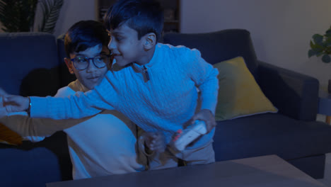 Two-Young-Boys-At-Home-Fighting-Over-Controllers-Playing-On-Computer-Games-Console-On-TV-Late-At-Night-2